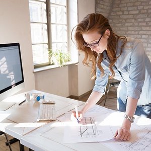 Eine Frau steht an einem Bürotisch und makiert eine Technische Zeichnung