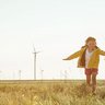 Eine Wiese auf dem zwei kleine Kinder rennen, im Hintergrund ist ein Windpark zu sehen